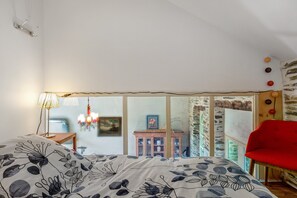Ein Schlafzimmer mit einem Bett, einem roten Sessel, einer Chandelüster und Blick durch eine Glastür.