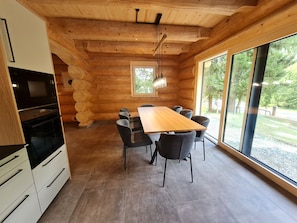 Een modern ingericht blokhutinterieur met een eethoek, inbouwapparatuur en grote ramen.
