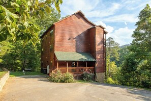A log cabin with a green roof, a porch, and a driveway leading to the entrance. - 👨‍👩‍👧‍👦 Sleeps 24 | 2 Hot Tubs | Game Room | Elevator | 3.3 mi to Dollywood (Sevierville)