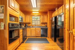 A wooden cabin kitchen with a black refrigerator, stove, and microwave. - 👨‍👩‍👧‍👦 Sleeps 24 | 2 Hot Tubs | Game Room | Elevator | 3.3 mi to Dollywood (Sevierville)