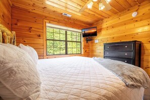 Ein Schlafzimmer einer Holzhütte mit einem Bett, einem Schminktisch, einem Fernseher und einem großen Fenster.
