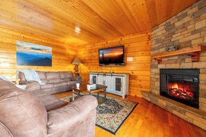 Ein gemütliches Blockhaus-Interieur mit Kamin, Holzwänden, einer Couch, einem Fernseher und einem Gemälde.
