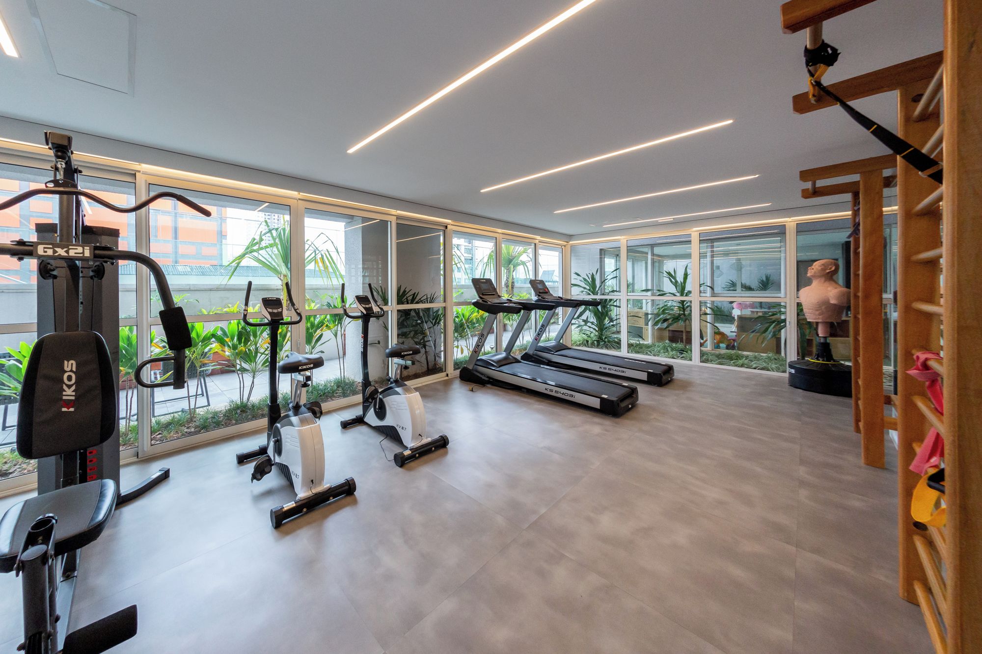 Ein modernes Fitnessstudio mit Cardiogeräten, Krafttrainingsgeräten und großen Fenstern mit Blick auf Grünflächen.