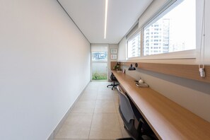 A modern office space with a long desk, a chair, and a window with a view of buildings. - Just by Bhomy (São Paulo)