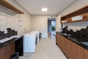 A hotel laundry room with a washing machine, a sink, and a trash bin. - Just by Bhomy (São Paulo)