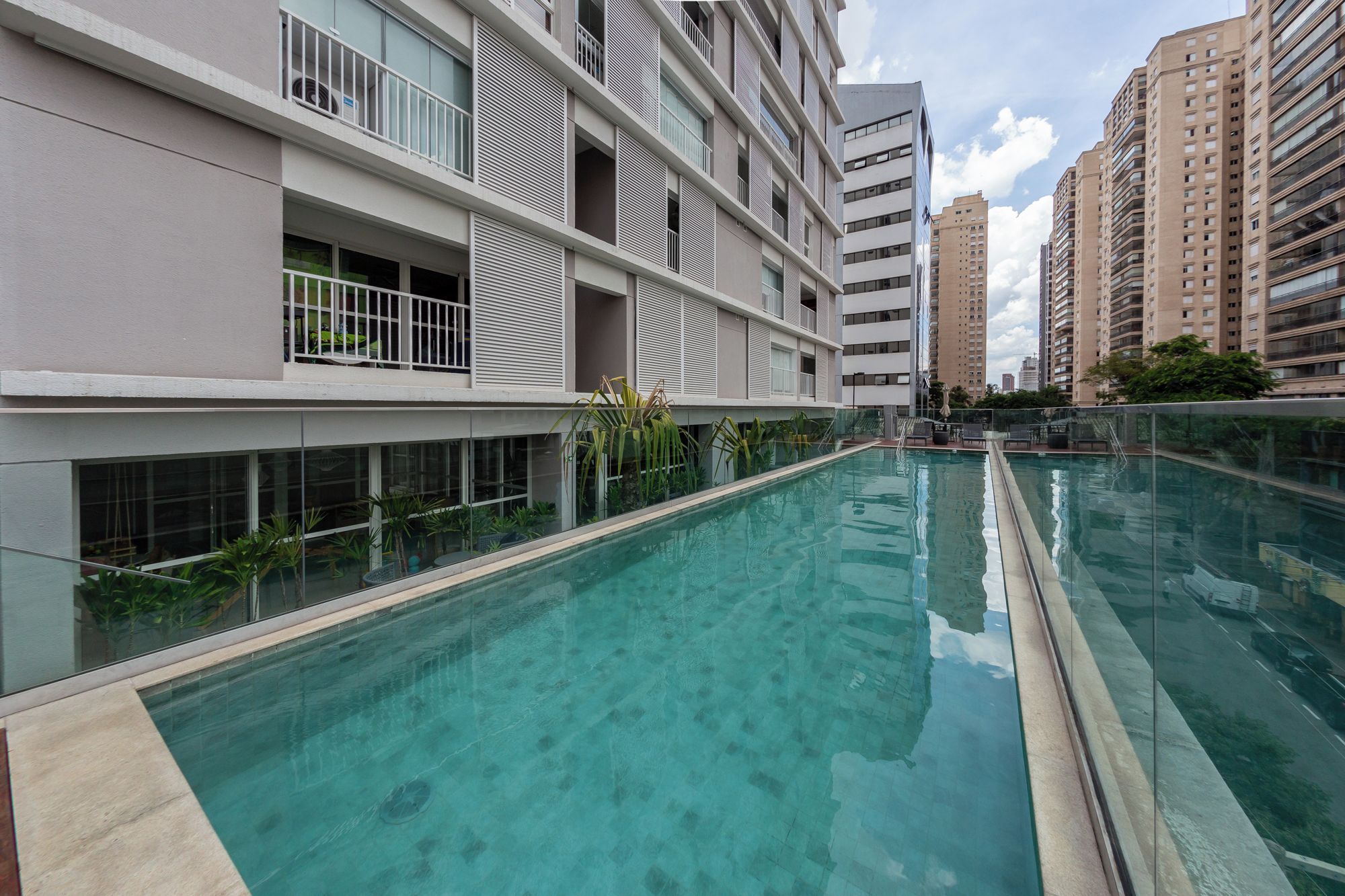 A modern residential building with a swimming pool, balconies, and a view of surrounding high-rise buildings.