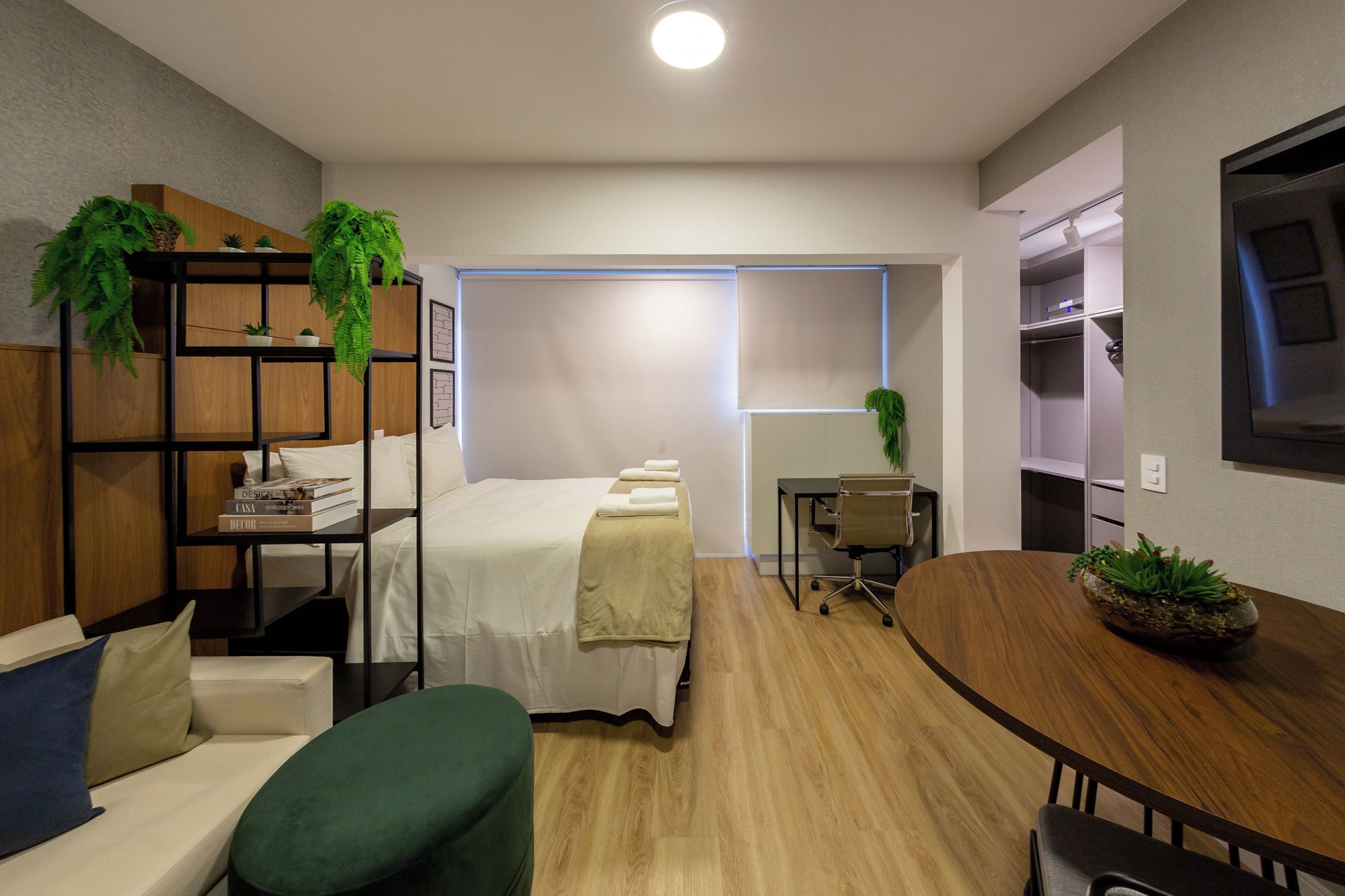 Ein modernes Hotelzimmer mit einem Bett, einer Sitzecke mit Tisch, einem Schreibtisch und einem Bücherregal.
