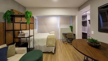 Ein modernes Hotelzimmer mit einem Bett, einer Sitzecke mit Tisch, einem Schreibtisch und einem Bücherregal.