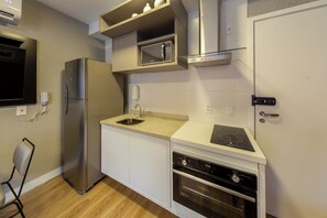 A compact kitchen with a built-in oven, a microwave, and a stainless steel refrigerator. - Just by Bhomy (São Paulo)