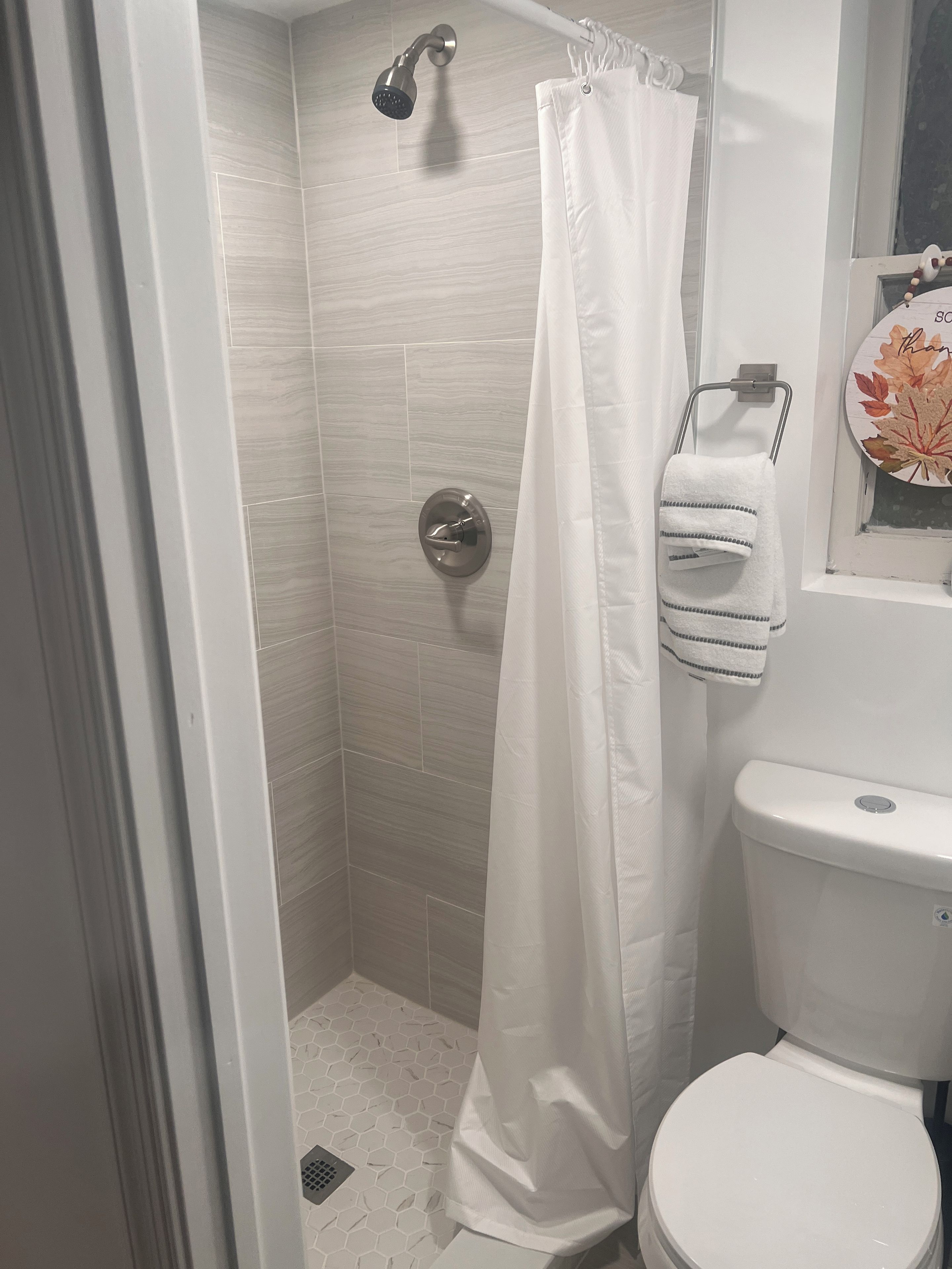 Een badkamer met een douche, toilet en een handdoekrek met een opgevouwen handdoek.