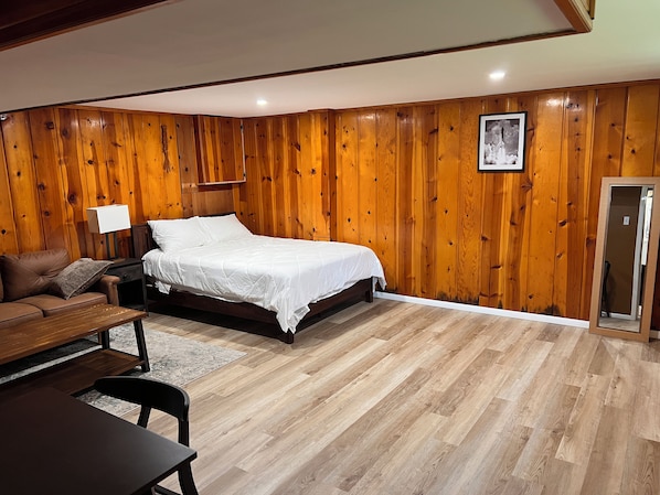 A bedroom with a wooden paneled wall, a bed, a nightstand, a desk, and a chair. - Brand-New, Newly Renovated Private Suite (Washington)