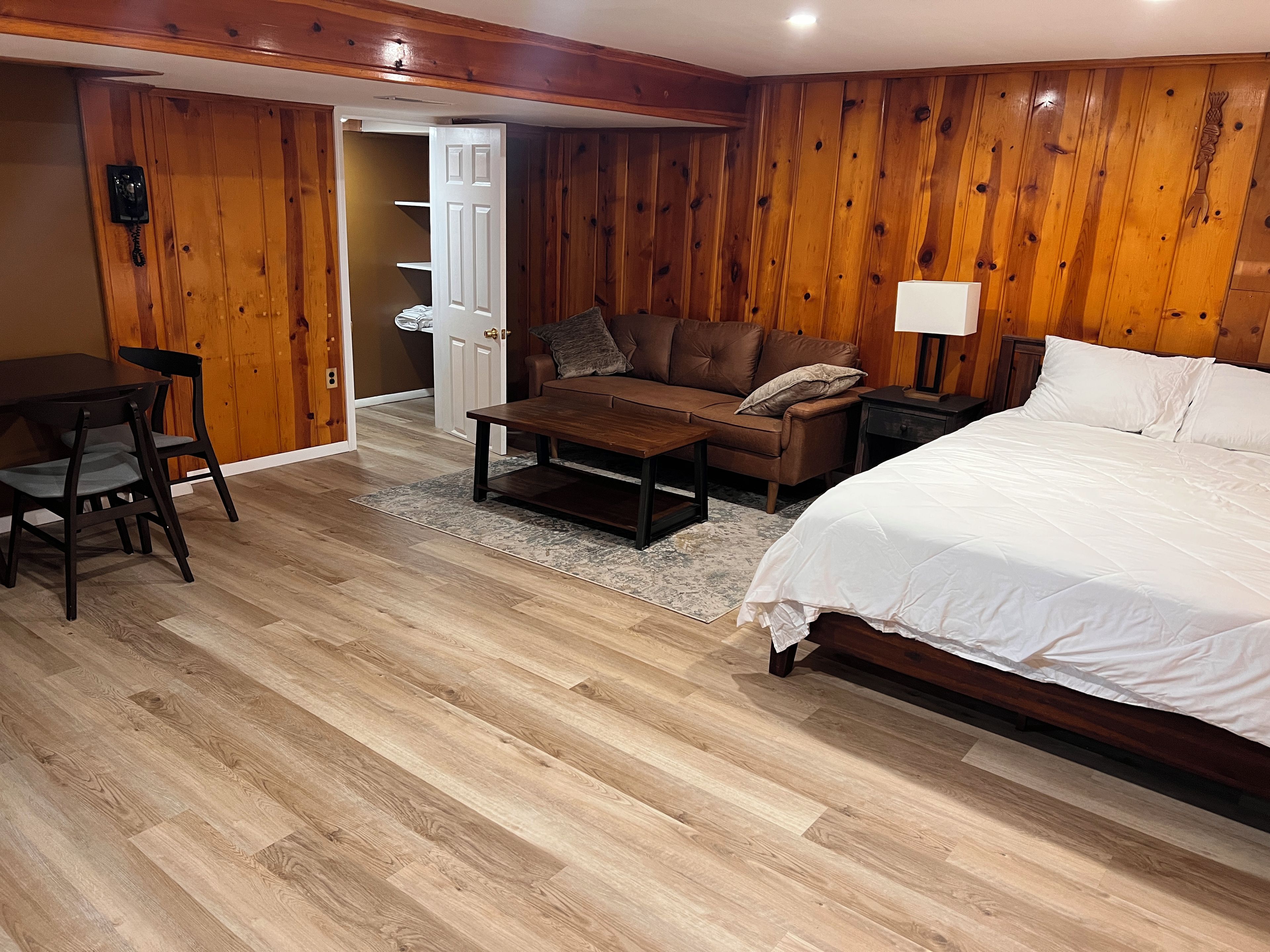 Quarto com cama, sofá, mesa de centro, escrivaninha e paredes de madeira.