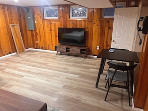 Een kamer met houten wanden, een televisie op een houten dressoir, een eettafel met stoelen en een deur met een telefoon.