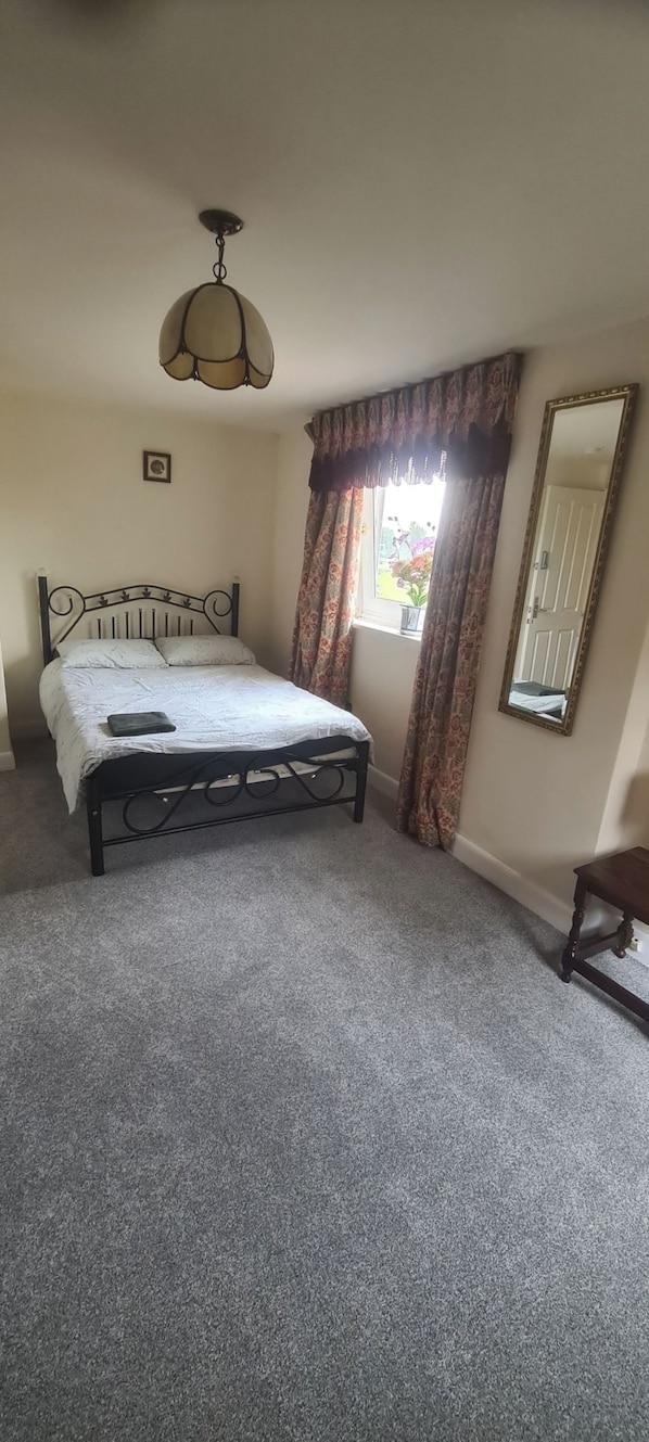 A bedroom with a bed, a ceiling fan, a window with curtains, a mirror, and a small table.