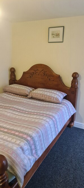 A bed with a patterned bedspread and two pillows, a wooden headboard, and a framed picture on the wall.
