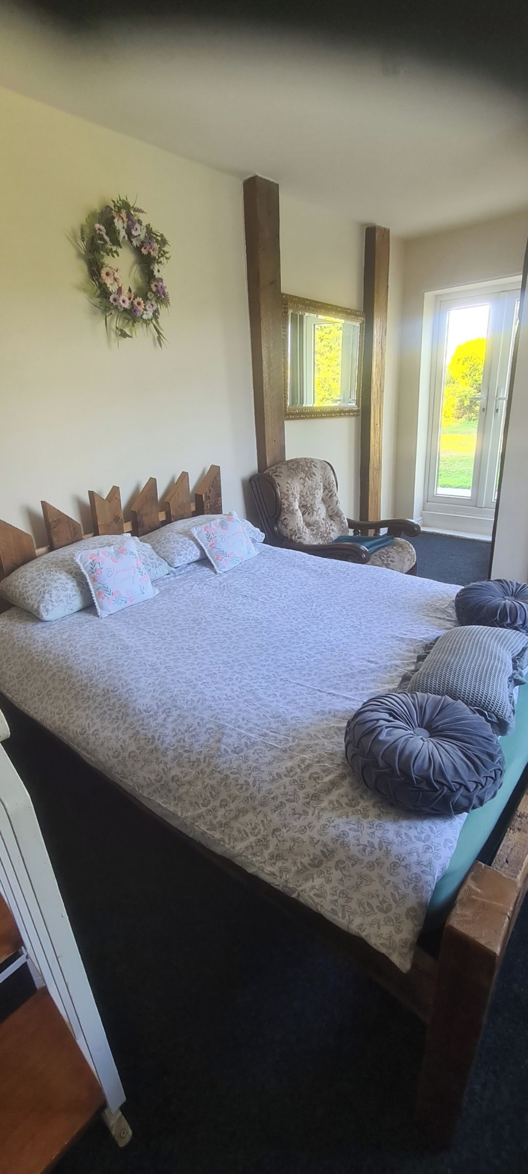 Une chambre à coucher avec un grand lit, une chaise, une fenêtre et un miroir fixé au mur.
