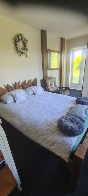 A bedroom with a large bed, a chair, a window, and a wall-mounted mirror.