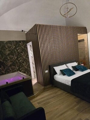Un dormitorio con cama, mesita de noche, sofá, televisor montado en la pared y un separador de madera con listones.