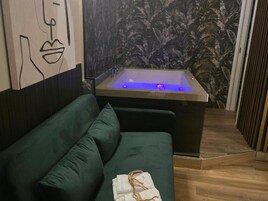 A room with a green sofa, a bathtub with blue lighting, and a wall with a floral pattern.