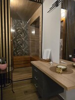 A modern bathroom with a wooden vanity, a glass shower enclosure, and a potted plant.