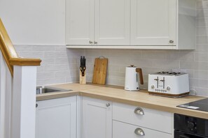 A kitchen with white cabinets, a wooden countertop, a toaster, and a cutting board. - Host & Stay | Temperance Mews (Saltburn)