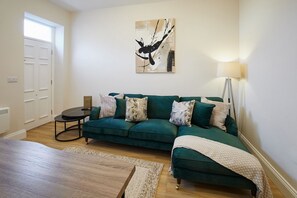 Una sala de estar con un sofá verde, una mesa de centro, una lámpara y un cuadro en la pared.
