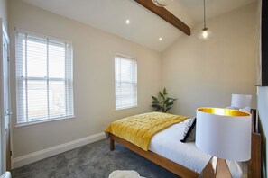 Een slaapkamer met een bed, twee ramen, een plant en een lamp.