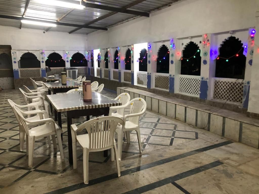 Un comedor con una mesa larga y sillas, suelo de baldosas y arcos decorativos con luces de adorno.