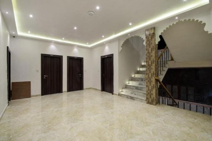 Una habitación espaciosa con piso de mármol, una escalera con barandilla decorativa y tres puertas de madera oscura.