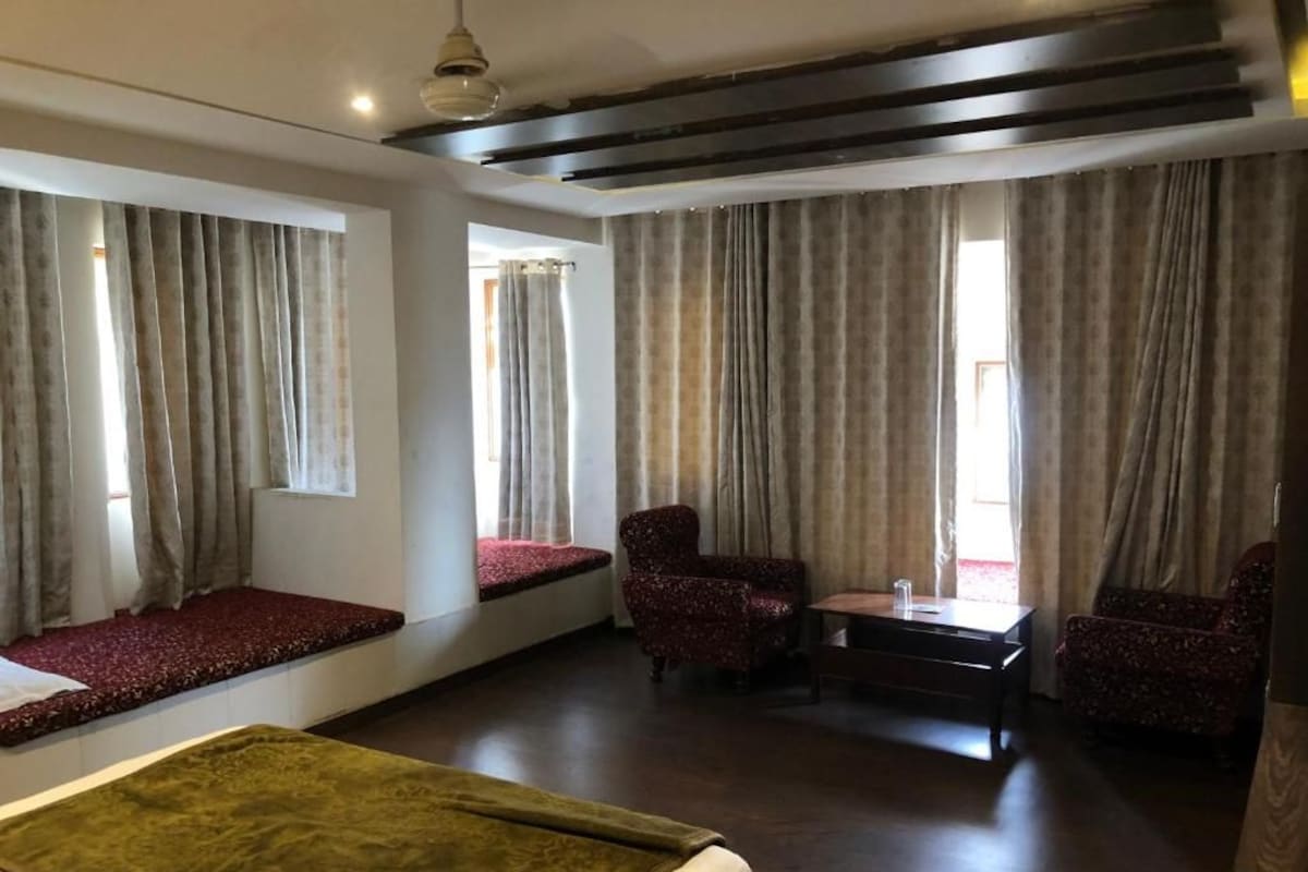 Una habitación de hotel con cama, zona de estar, dos sillones, una mesita y cortinas.