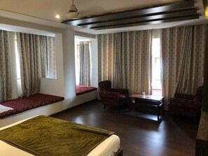 A hotel room with a bed, seating area, two armchairs, a small table, and curtains. - Hotel Rani Palace (Udaipur)