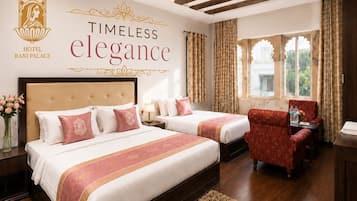 A hotel room with a large bed, two smaller beds, a red armchair, a wooden floor, and a ceiling fan.