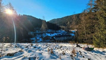 Schneebedeckte Landschaft mit einem Gebäude im Hintergrund, umgeben von Bäumen und Bergen.