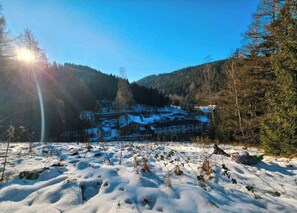 Paisagem coberta de neve com um edifício ao fundo, rodeada por árvores e montanhas.