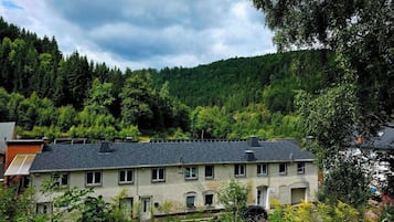 A two-story building with a sloped roof, surrounded by dense greenery and trees.