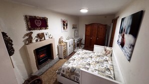 Ein gemütliches Schlafzimmer mit Kamin, einem Bett mit gemustertem Überwurf, einem Schminktisch, einem Schreibtisch und einem Kleiderschrank.