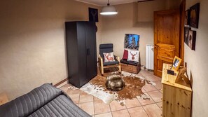 Ein Zimmer mit einer Couch, einem Sessel, einem Schrank, einem Kuhfellteppich und einem Holzkasten mit einem Bilderrahmen.