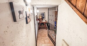 Ein schmaler Korridor mit Fliesenboden, einer Holztür rechts und einem Metallgitter links.