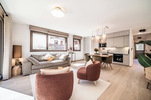 Ein geräumiger Wohnbereich mit Sofa, Hocker und Esstisch. Im Hintergrund ist eine Küche zu sehen.