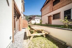 A wooden bench in a courtyard with a building on one side and a mountain in the background. - Laverock – Garden | Parking | Near Lifts | Morzine (Morzine)