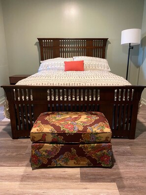 A bed with a patterned bedspread and pillows, a wooden bench with a floral cushion, and a bedside lamp.