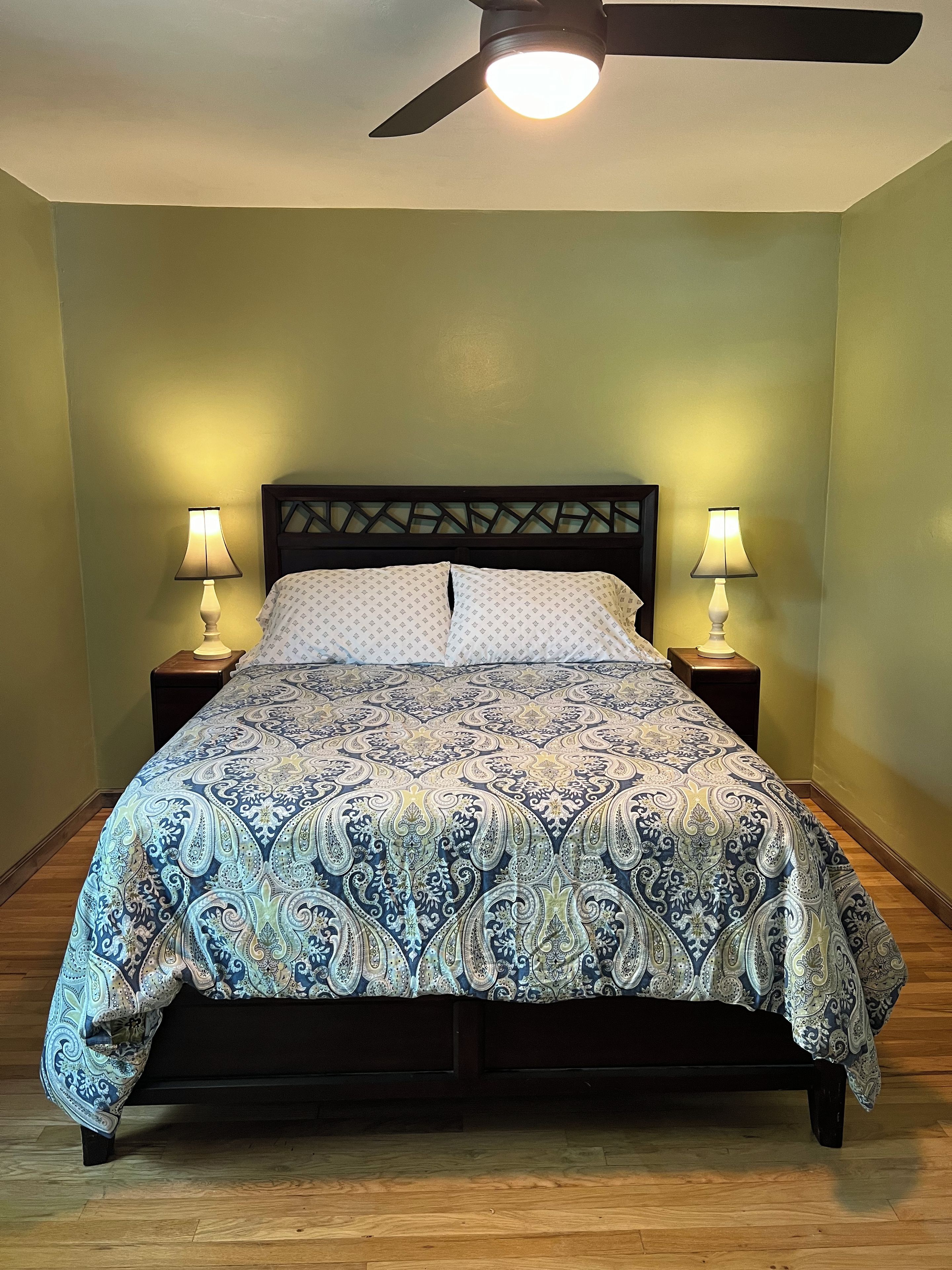 A bed with a patterned bedspread, two bedside lamps, and a ceiling fan.