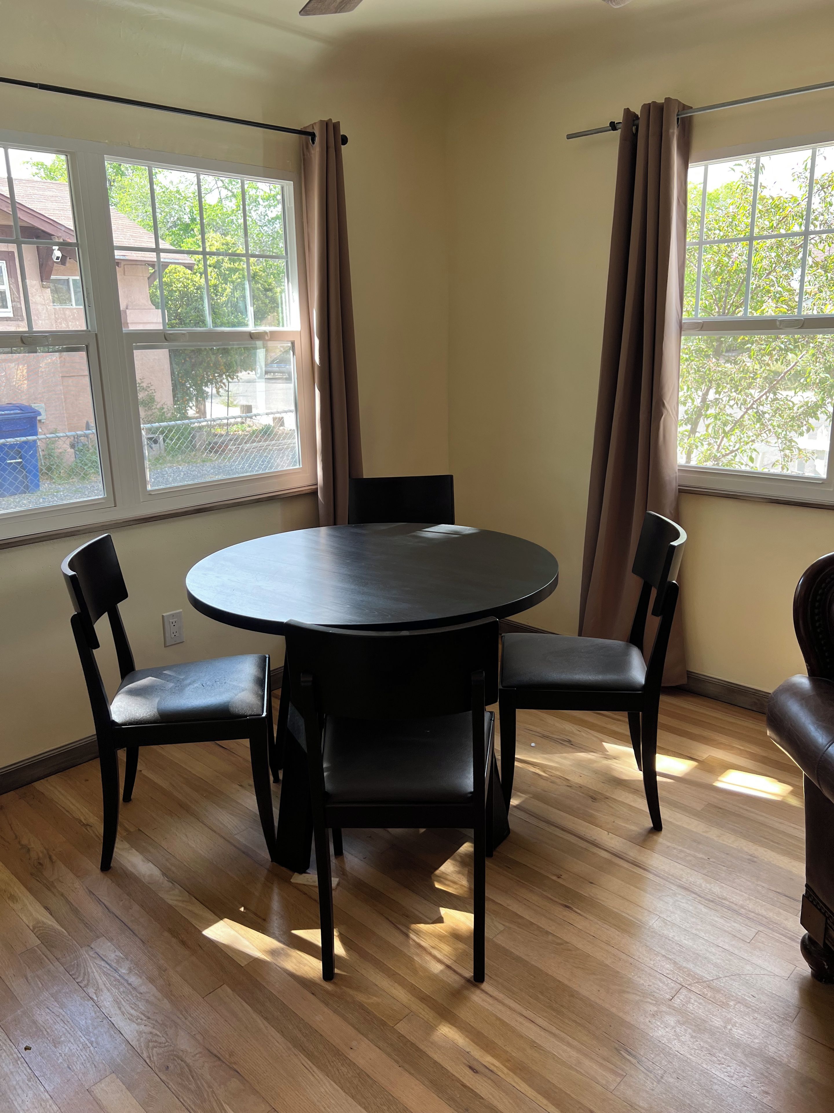 A room with a round table, two chairs, a ceiling fan, and large windows with curtains.