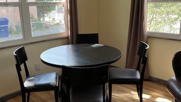 A room with a round table, two chairs, a ceiling fan, and large windows with curtains.