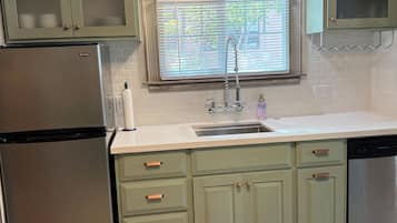A kitchen with a stainless steel refrigerator, a sink with a faucet, and green cabinets with glass doors.