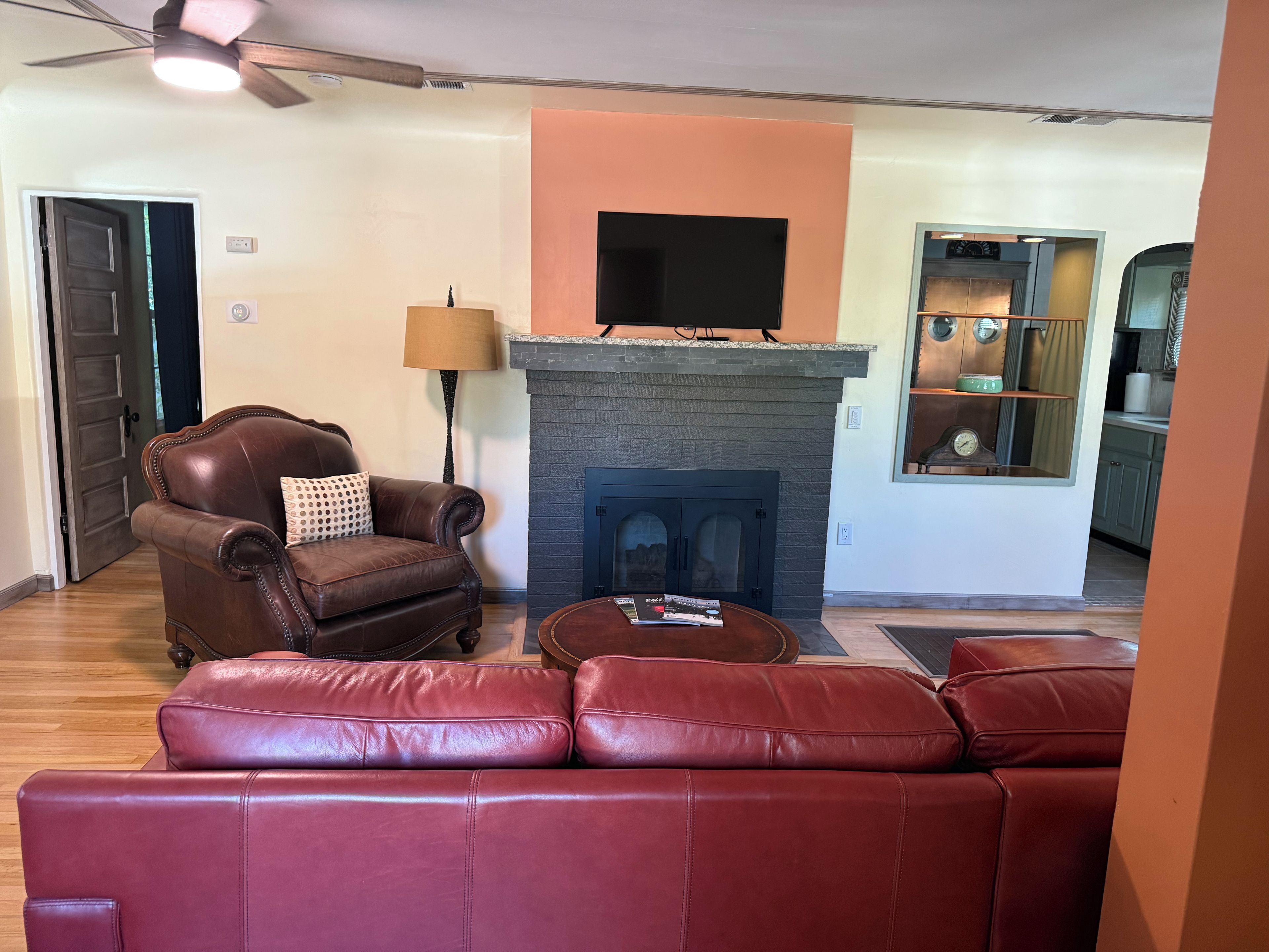 A living room with a fireplace, leather sofas, a television, and a kitchen area visible through an open door.