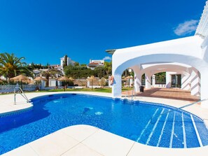 A swimming pool with a clear blue water surface, surrounded by a white structure with arches, and a view of a coastal town in the background. - AP178 Capistrano Playa 601 (Nerja)
