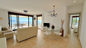 A spacious living room with a sofa, dining table, and chairs, large windows with a view of the sea, and a chandelier. - AP178 Capistrano Playa 601 (Nerja)
