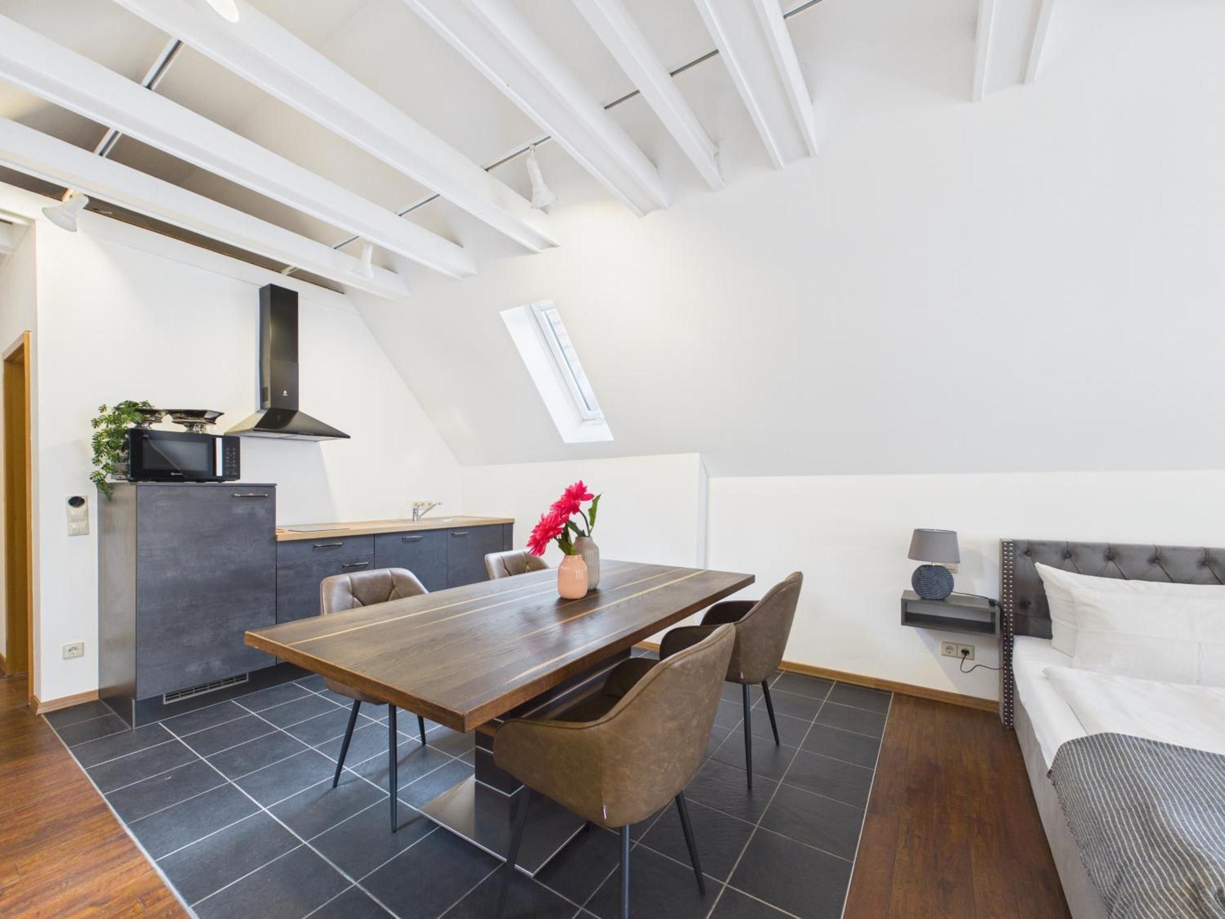 A modern loft-style living space with a dining area, kitchenette, and a loft bedroom.