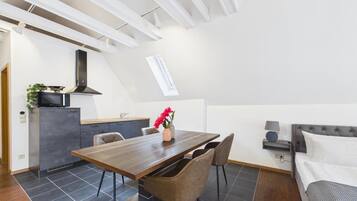 A modern loft-style living space with a dining area, kitchenette, and a loft bedroom.